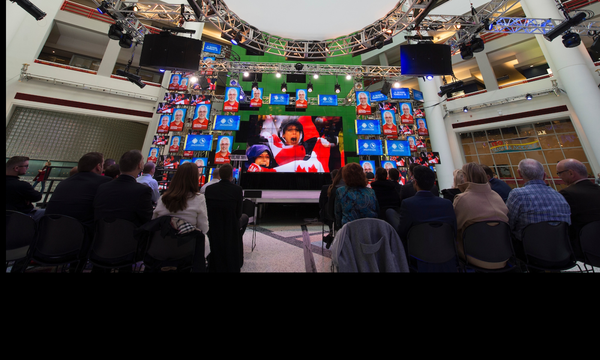 Des personnes en avant d'un écran géant de CBC