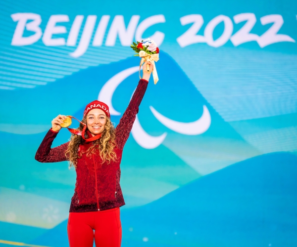 Natalie Wilkie smiling and holding her gold medal on the podium at the Beijing 2022 Paralympic Winter Games