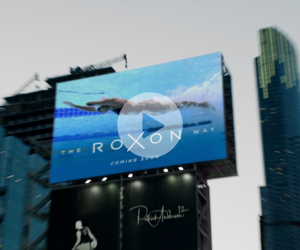 A still from the "We're Here" campaign showing a billboard promoting a documentary about Katarina Roxon