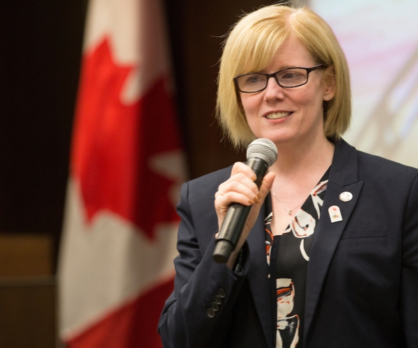 A smiling Carla Qualtrough speaking at an event holding a microphone
