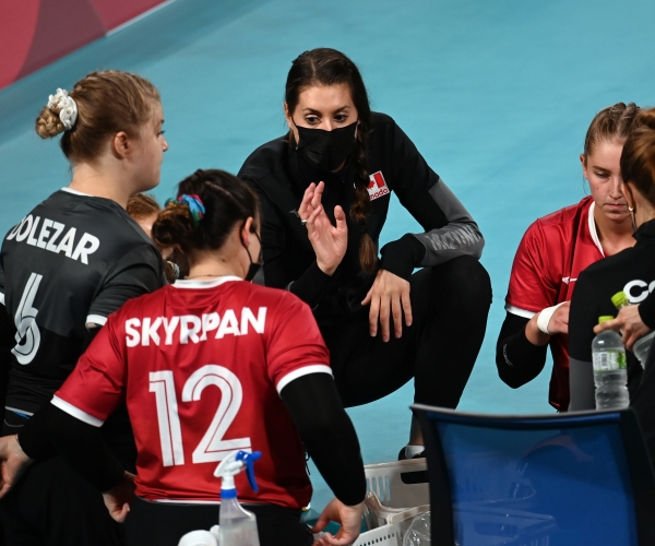 Head coach Nicole Ban kneeling down talking to the Canadian women's sitting volleyball team on the sidelines at the Tokyo 2020 Paralympic Games