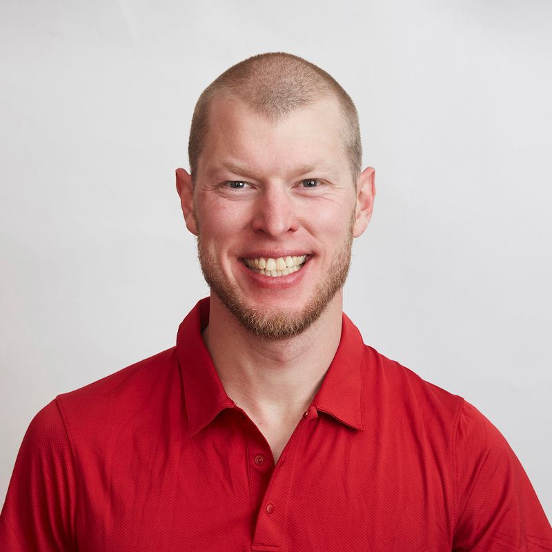 Portrait du paralympien canadien Mark Arendz souriant devant un fond blanc, portant une chemise rouge à col.