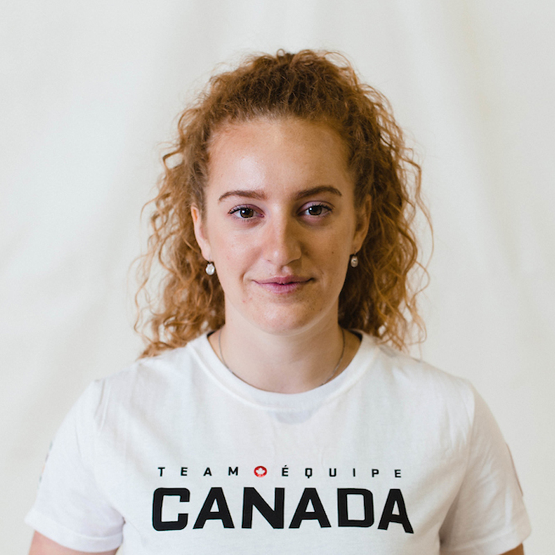 Portrait de Payden Vair, joueuse canadienne de volleyball assis, souriant doucement en portant un t-shirt blanc d’Équipe Canada sur un fond neutre.