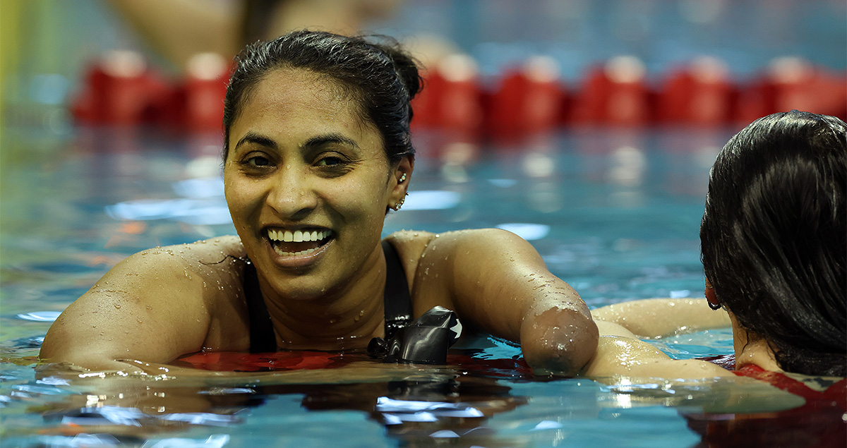 Canadian Para swimmer Katarina Roxon with a joyful expression emerges from the water in an indoor swimming pool, appearing tired but satisfied after a race. | La nageuse canadienne Katarina Roxon, à l'expression joyeuse, sort de l'eau dans une piscine couverte. Elle semble fatiguée mais satisfaite après une course.