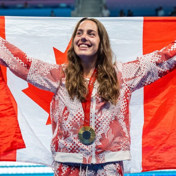 Para swimmer stands on podium holding canada flag behind her back