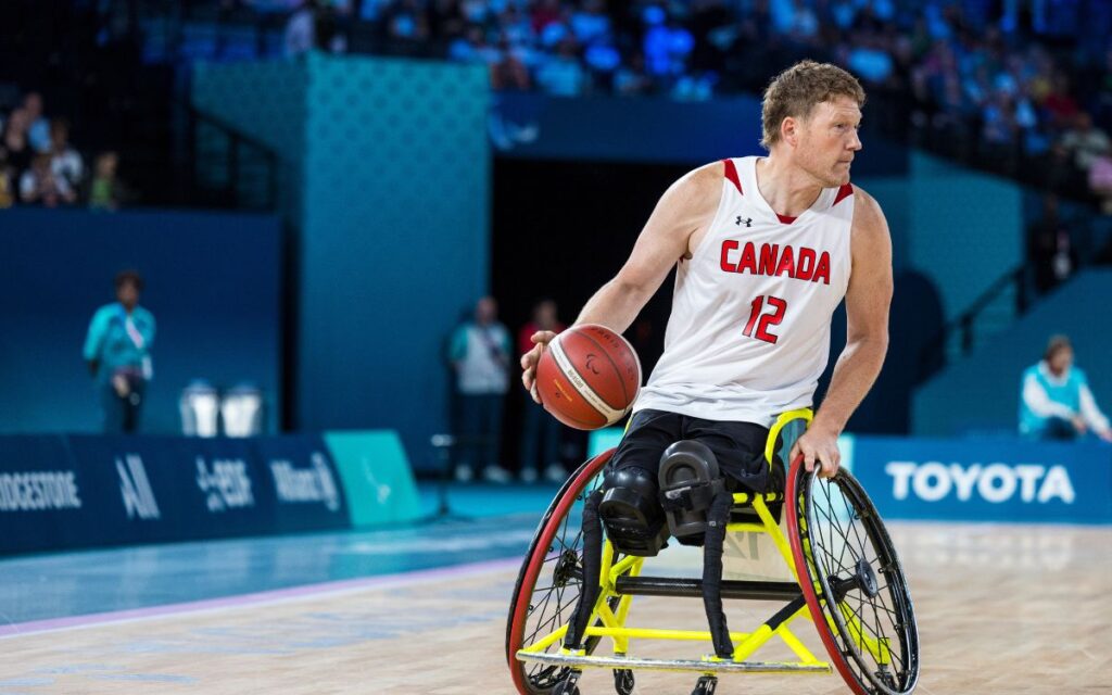 La star du basket-ball en fauteuil roulant Patrick Anderson fait rebondir le ballon.