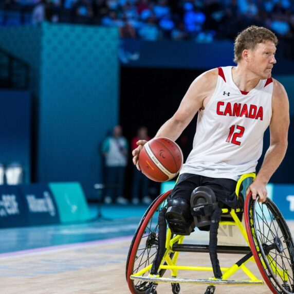 La star du basket-ball en fauteuil roulant Patrick Anderson fait rebondir le ballon.