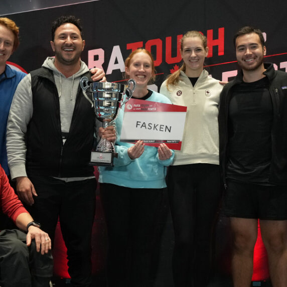 Les membres de l’équipe Fasken, gagnants de la ParaTough Cup de Vancouver, posent ensemble en souriant et tenant leur trophée. Le paralympien Josh Dueck est assis à l’avant dans un fauteuil roulant, portant un chandail rouge. Le groupe se tient devant un fond ParaTough.