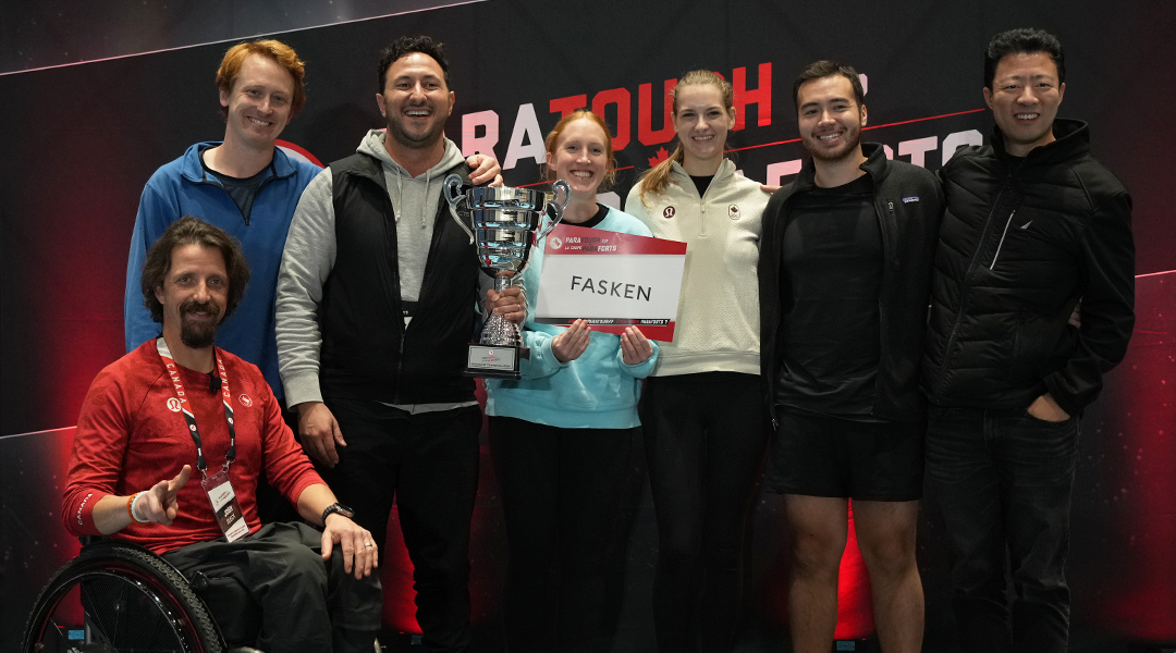 Les membres de l’équipe Fasken, gagnants de la ParaTough Cup de Vancouver, posent ensemble en souriant et tenant leur trophée. Le paralympien Josh Dueck est assis à l’avant dans un fauteuil roulant, portant un chandail rouge. Le groupe se tient devant un fond ParaTough.