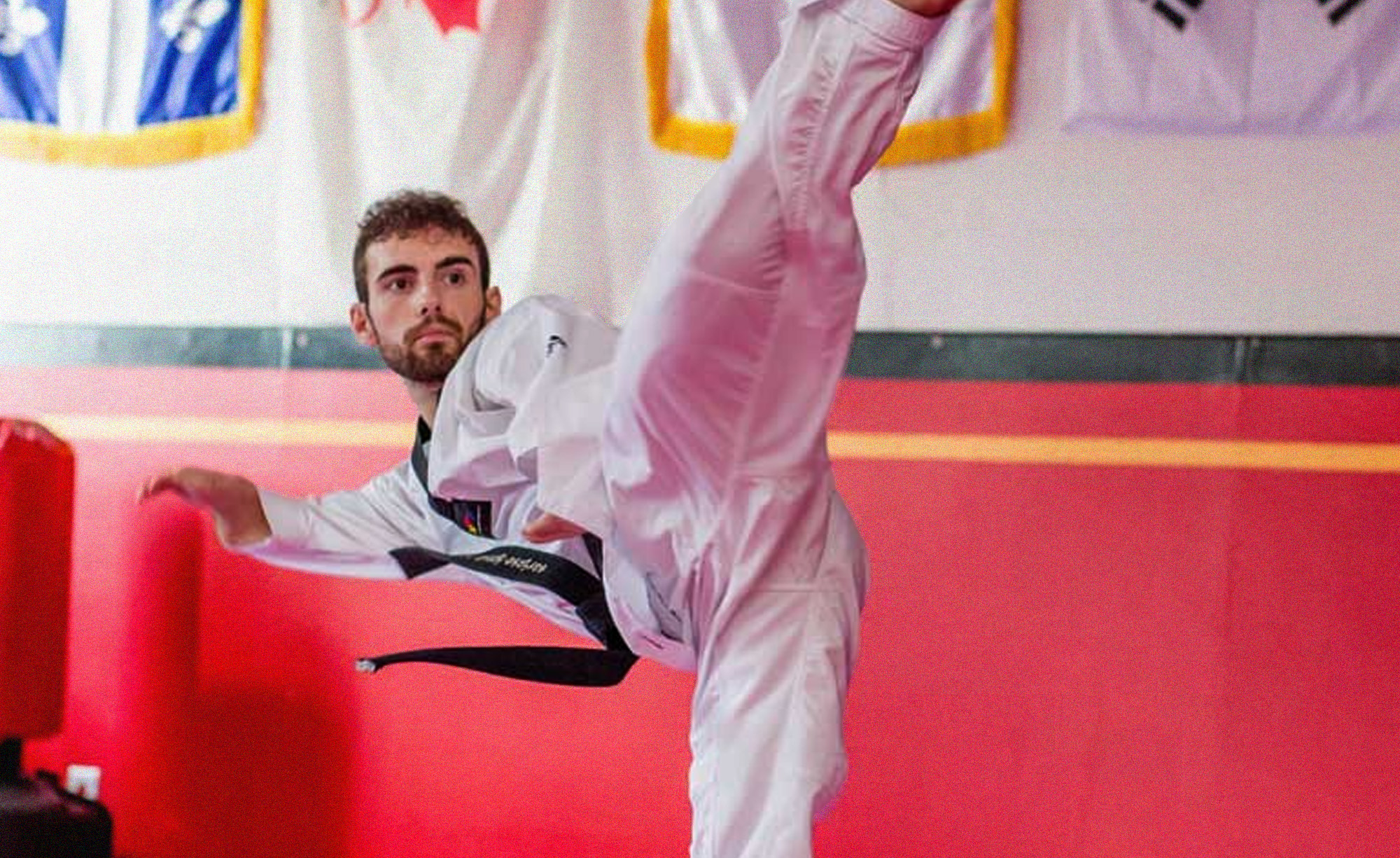 Anthony Cappello, athlète canadien de para-taekwondo, exécute un coup de pied haut dans un dojo, vêtu d’un uniforme blanc de taekwondo et d’une ceinture noire. Les drapeaux du Canada et du Québec sont visibles en arrière-plan, représentant ses origines canadiennes.