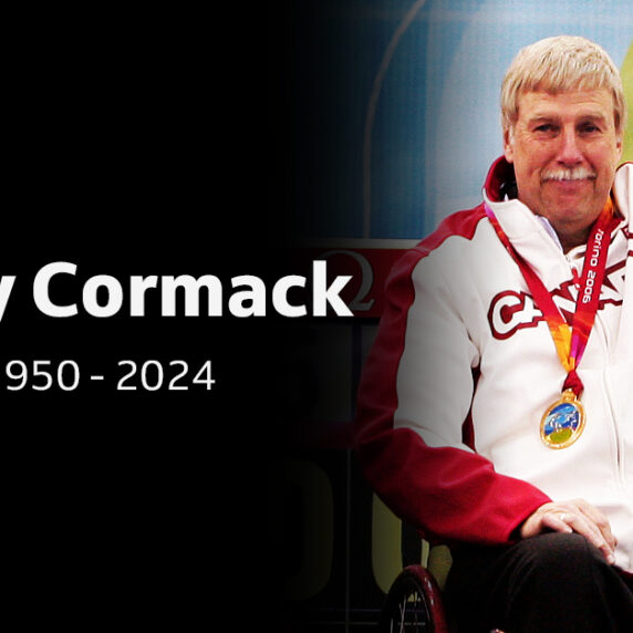 Portrait du paralympien canadien Gary Cormack, 1950-2024, portant une veste de l'équipe du Canada et une médaille, levant le bras en signe de célébration.