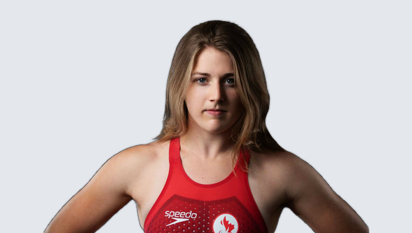 Canadian Paralympian Abi Tripp, a Para swimmer, wearing a red Team Canada Speedo swimsuit with the Canadian Paralympic logo. She stands confidently with her hands on her hips, gazing directly at the camera with a determined expression. Her wavy, shoulder-length blonde hair frames her face.