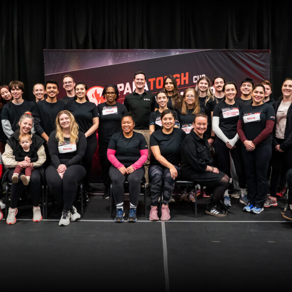 Une photo de groupe du personnel de Petro-Canada et des paralympiens canadiens lors de l'événement ParaTough Cup à Calgary. Les participants sont rassemblés devant une toile de fond noire et rouge avec le logo ParaTough Cup, souriant et posant ensemble. Certaines personnes sont assises, y compris des athlètes en fauteuil roulant, tandis que d'autres se tiennent debout derrière eux. Le groupe reflète une diversité d'âges, d'origines et de rôles, uni dans son soutien au para sport.