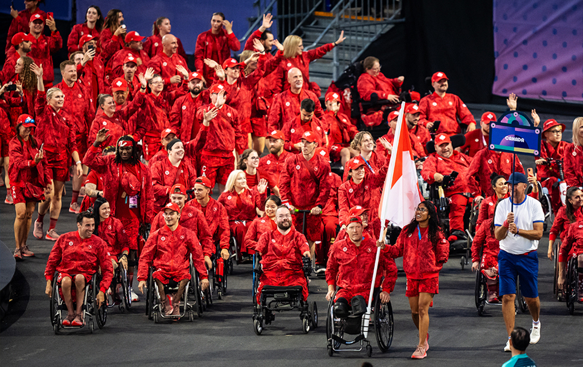 L’équipe paralympique canadienne fait son entrée dans le stade lors de la cérémonie d’ouverture des Jeux paralympiques de Paris 2024. Vêtus de tenues rouges assorties arborant des feuilles d’érable blanches, les athlètes paralympiques canadiens sourient et saluent la foule avec fierté, une athlète portant le drapeau canadien à l’avant de la délégation.