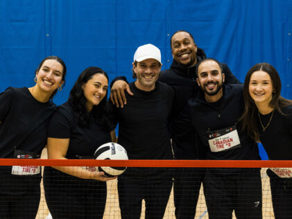 Une équipe souriante de Canadian Tire pose ensemble sur un terrain de gymnase derrière un filet lors de l'événement ParaTough Cup à Toronto, tenant un ballon de volleyball et vêtue de chandails noirs assortis.