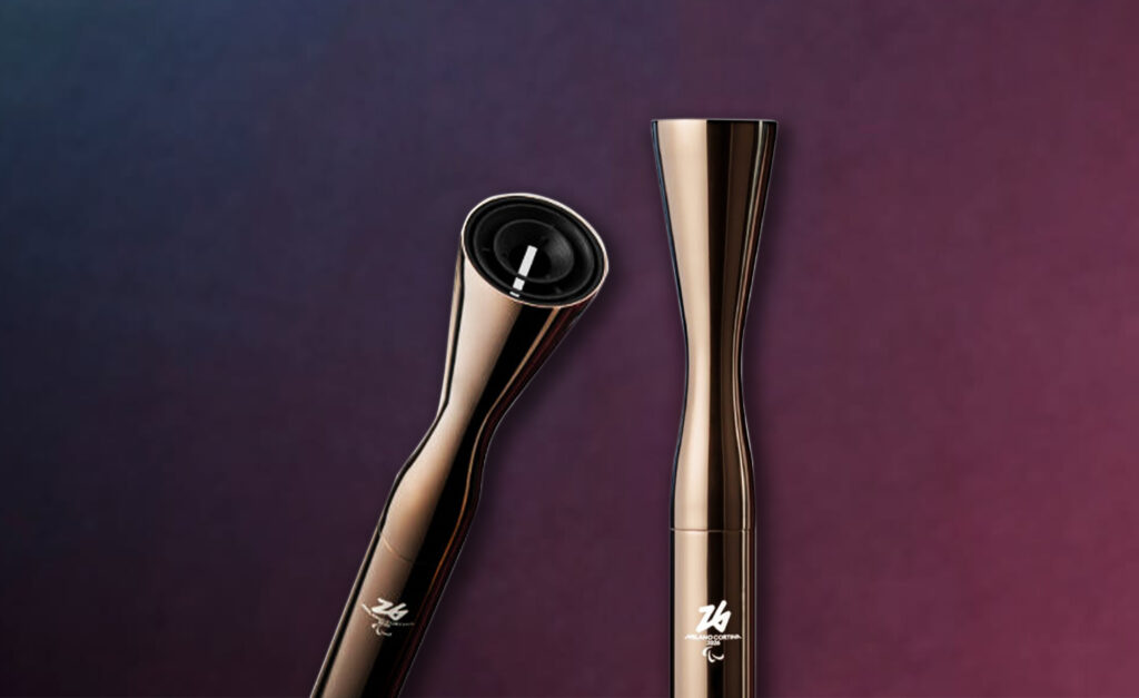 Deux vues de la torche des Jeux paralympiques d’hiver de Milano Cortina 2026, présentant un design métallique élégant avec les logos officiels de Milano Cortina 2026 et des Jeux paralympiques sur un fond dégradé.