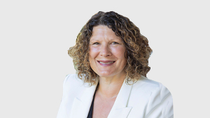 Brenda Plowman, directrice au Comité paralympique canadien, sourit en portant un blazer blanc et un haut noir sur un fond gris pâle.