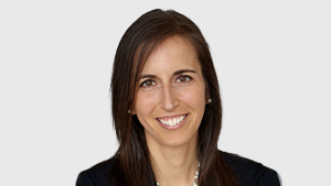 Dominique Breton, Director at the Canadian Paralympic Committee, smiles while wearing a dark blazer and pearl necklace against a light grey background.