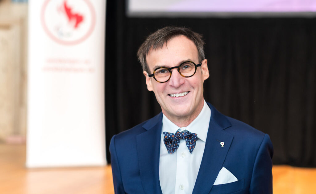 Marc-André Fabien, président du Comité paralympique canadien, sourit en portant un complet bleu marine, un nœud papillon à motifs et des lunettes lors d’un événement officiel.