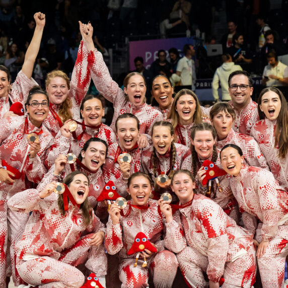 L’équipe canadienne féminine de volleyball assis célèbre ensemble en tenue paralympique rouge et blanche, brandissant fièrement leurs médailles de bronze de Paris 2024 et les mascottes, tout sourire et unies dans la joie.