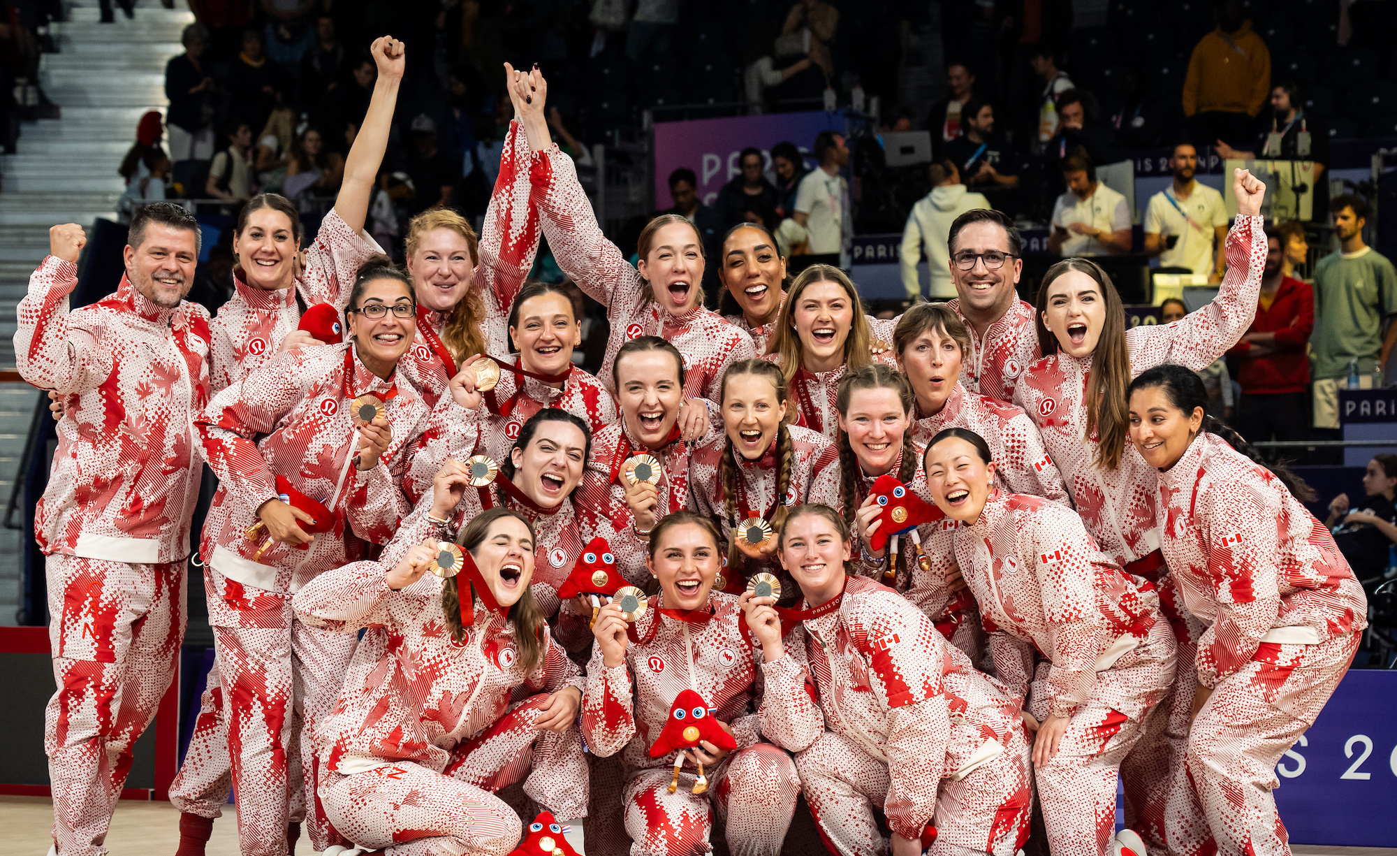 L’équipe canadienne féminine de volleyball assis célèbre ensemble en tenue paralympique rouge et blanche, brandissant fièrement leurs médailles de bronze de Paris 2024 et les mascottes, tout sourire et unies dans la joie.