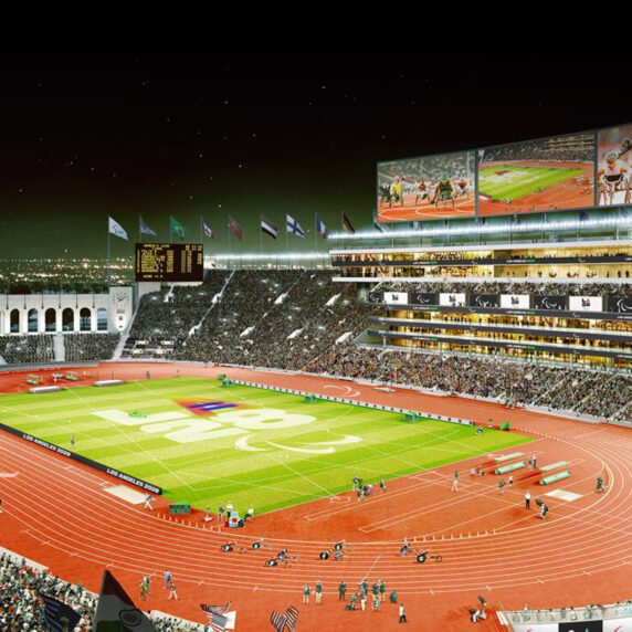 Rendu nocturne du Los Angeles Memorial Coliseum illuminé pour les Jeux paralympiques de LA28, avec un stade plein à craquer, le symbole paralympique au centre du terrain, des drapeaux flottant au sommet et de grands écrans diffusant des épreuves d’athlétisme paralympique.