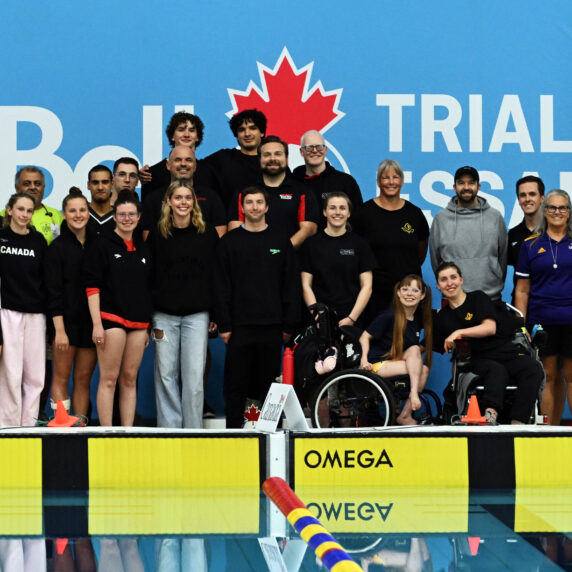 Photo de groupe de l’équipe paranatation et du personnel de Natation Canada sur le bord de la piscine devant une bannière bleue des « Essais Bell », avec les athlètes et entraîneurs souriants.