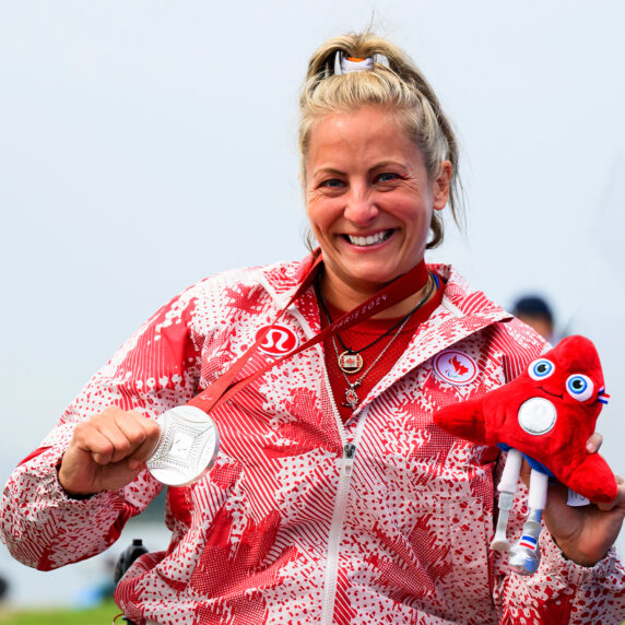 Brianna Hennessy sourit fièrement en tenant sa médaille d’argent de Paris 2024 et la peluche rouge de la mascotte paralympique, vêtue de sa veste d’Équipe Canada ornée de feuilles d’érable.