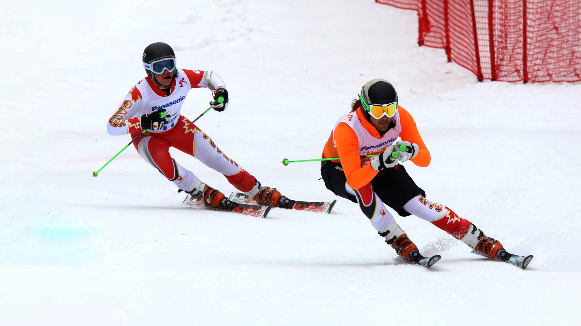 Le skieur para-alpin canadien Mac Marcoux (à gauche) suit son guide lors d’une épreuve de ski pour athlètes ayant une déficience visuelle aux Jeux paralympiques d’hiver de Sotchi 2014. Tous deux portent des combinaisons de course aux couleurs du Canada, effectuant une descente synchronisée sur la piste enneigée.