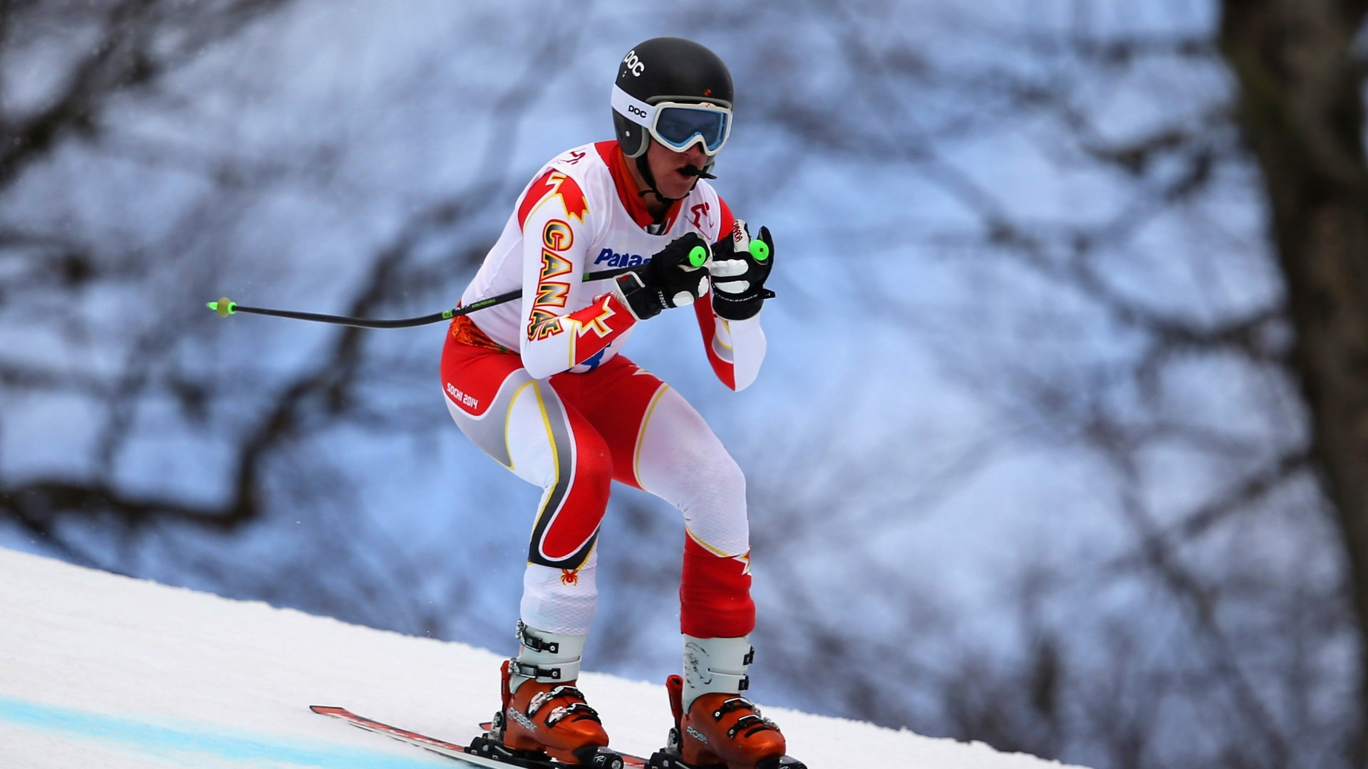 Le skieur para-alpin canadien Mac Marcoux participe à une épreuve de descente aux Jeux paralympiques d’hiver de Sotchi 2014, vêtu d’une combinaison de vitesse rouge et blanche d’Équipe Canada, d’un casque et de lunettes de ski, en position de recherche de vitesse sur la piste enneigée.