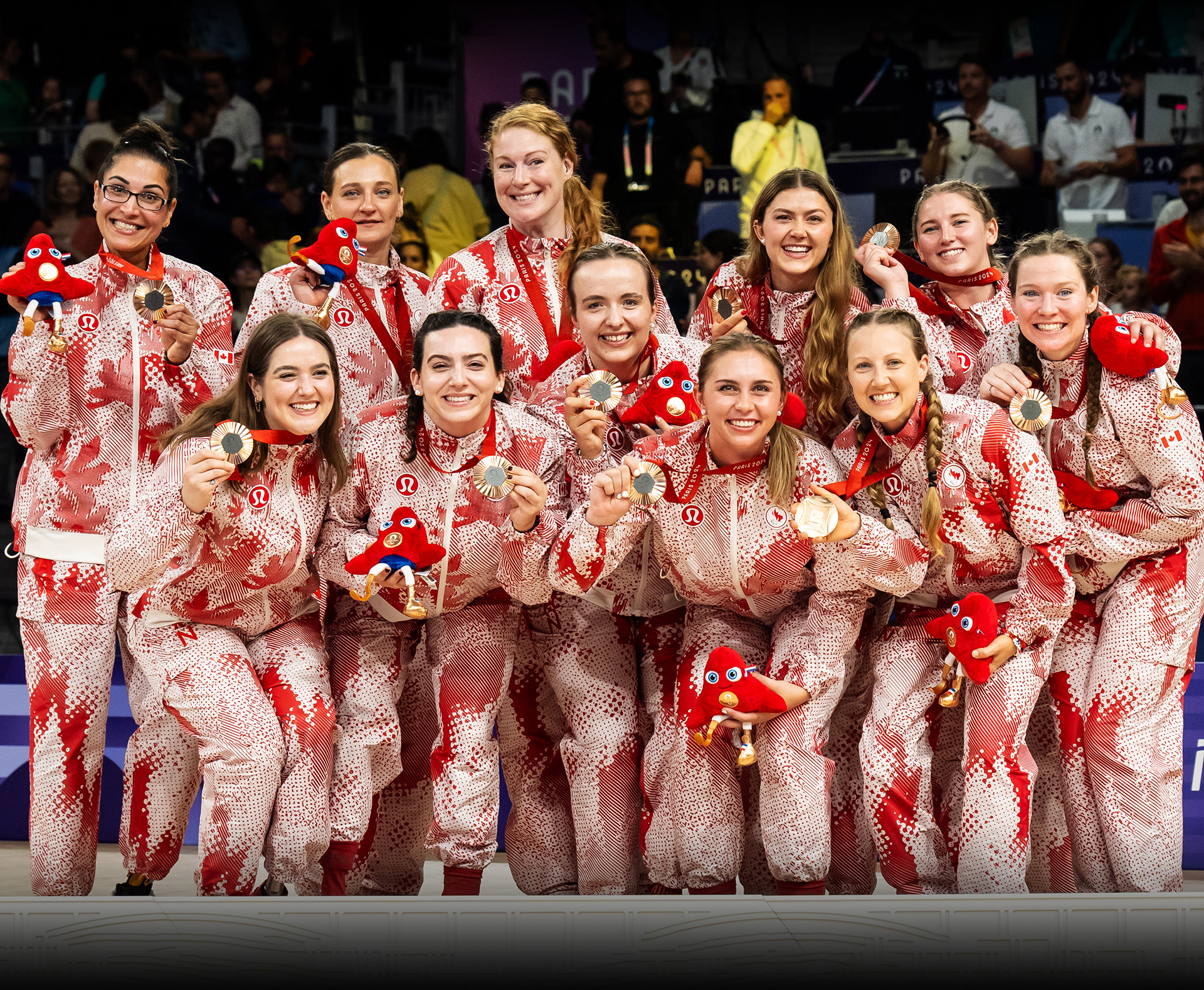 L’équipe canadienne féminine de volleyball assis célèbre sa médaille de bronze aux Jeux paralympiques de Paris 2024. Les athlètes portent des uniformes rouges et blancs de l’équipe canadienne conçus par Lululemon et tiennent des mascottes paralympiques en peluche tout en souriant fièrement.