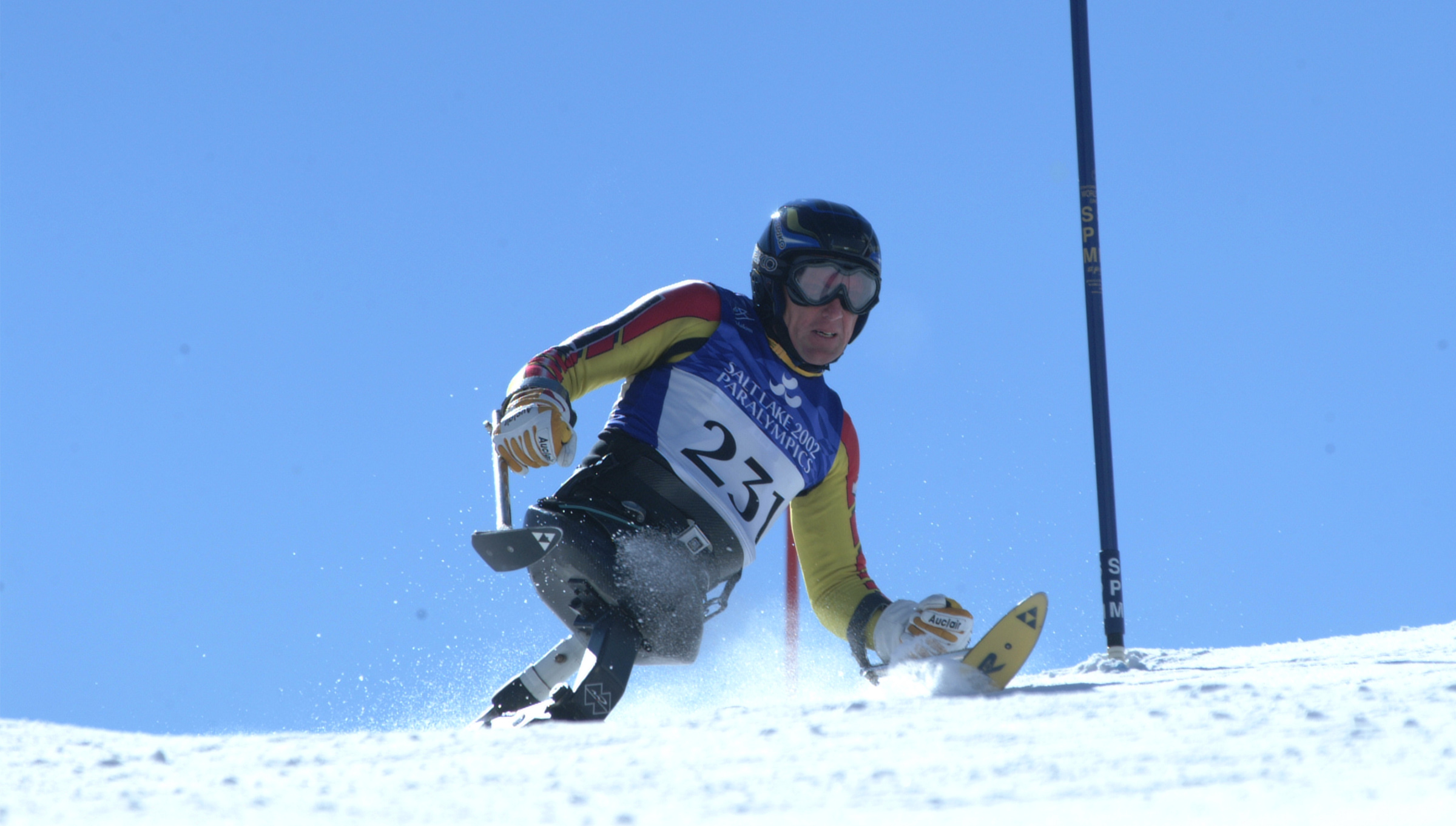 Le skieur canadien de para-alpinisme Daniel Wesley dévale la pente en monoski aux Jeux paralympiques d’hiver de Salt Lake City 2002, portant le dossard 231 et un gilet de course bleu.