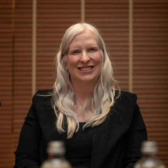 La paralympienne canadienne Chelsey Gotell sourit en étant assise à une table de conférence, portant un veston noir et arborant de longs cheveux blonds, lors d’un événement officiel.