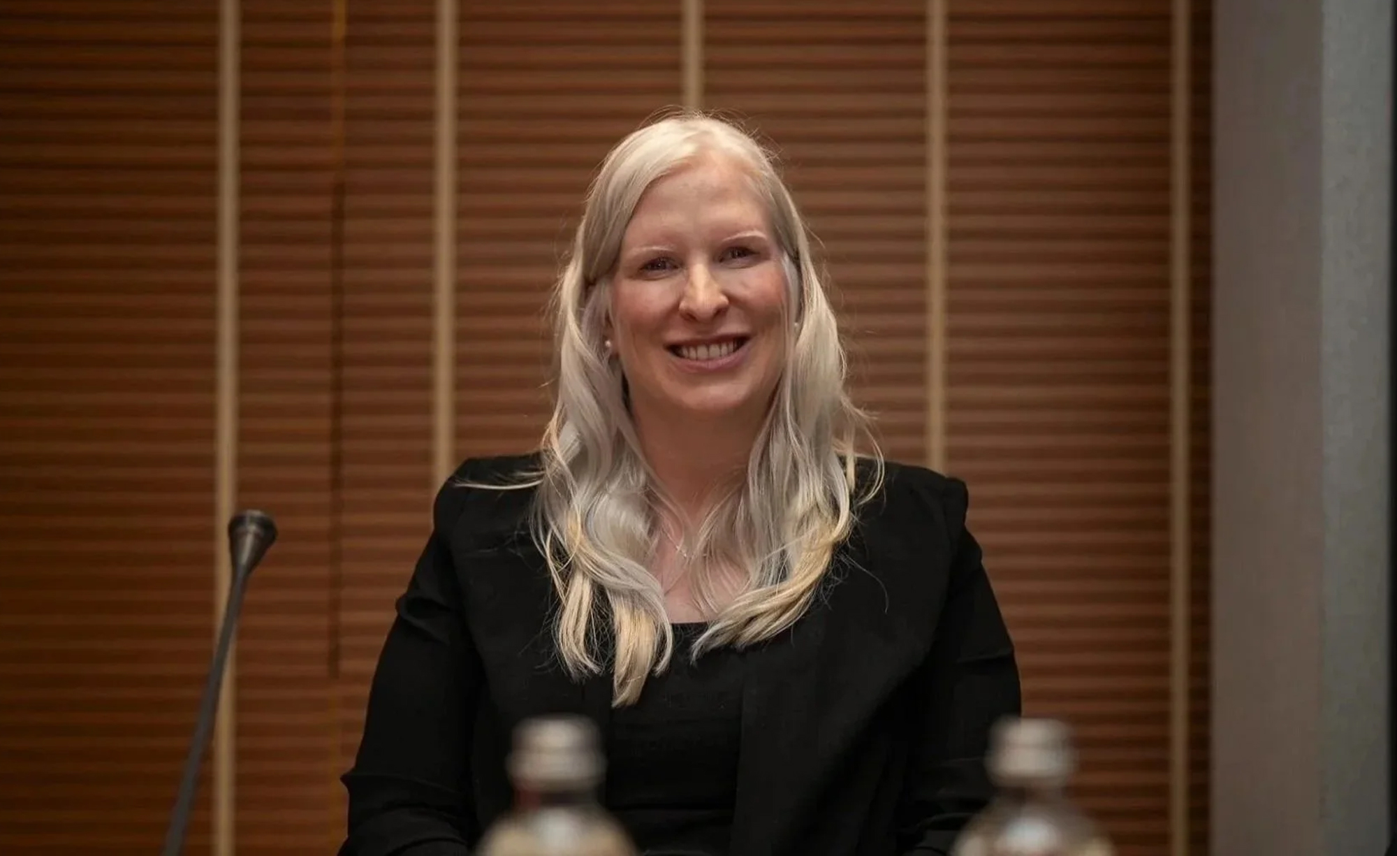 La paralympienne canadienne Chelsey Gotell sourit en étant assise à une table de conférence, portant un veston noir et arborant de longs cheveux blonds, lors d’un événement officiel.