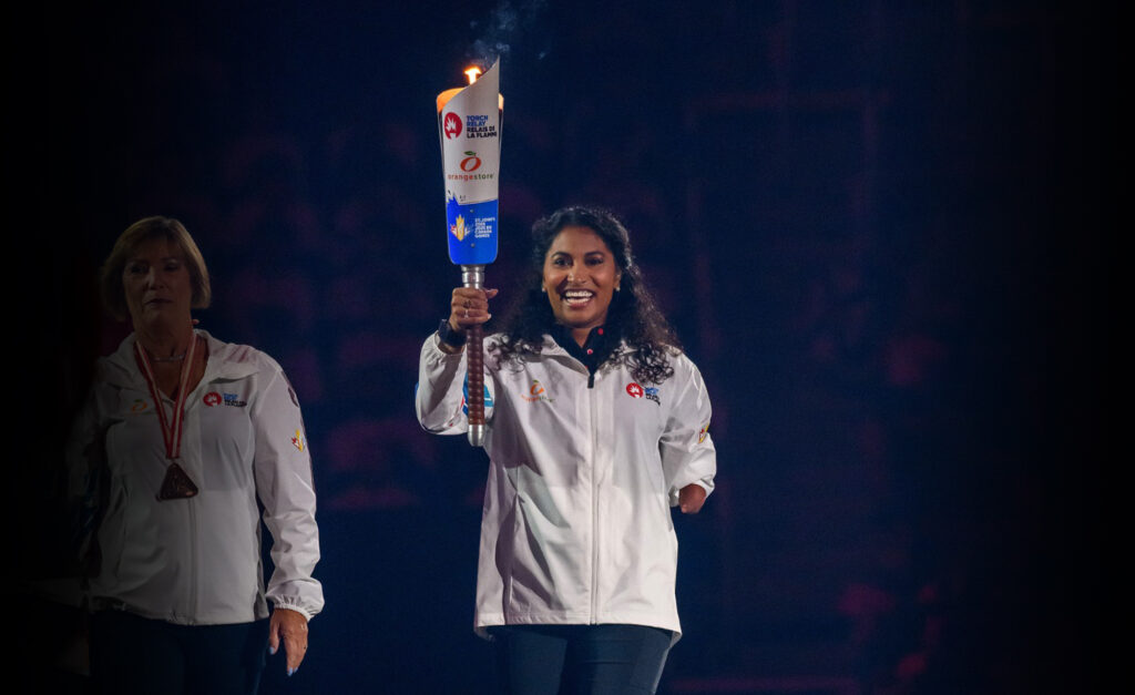 La paranageuse canadienne Katarina Roxon sourit en tenant fièrement la flamme allumée lors de la cérémonie d’ouverture des Jeux du Canada 2025. Elle porte une veste blanche de l’équipe de Terre-Neuve-et-Labrador.