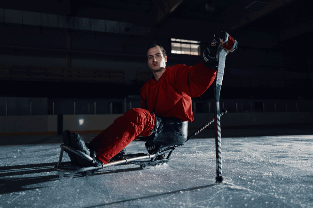 Silhouette de l’athlète canadienne de ski para-alpin Mollie Jepsen en plein saut pendant un exercice d’entraînement dans son garage. L’intérieur du garage est illuminé d’une lumière orange chaleureuse, en contraste avec la soirée bleutée à l’extérieur. Son ombre s’étire sur l’entrée alors qu’elle saute sur un caisson d’entraînement, entourée de vélos, d’équipement et de matériel.