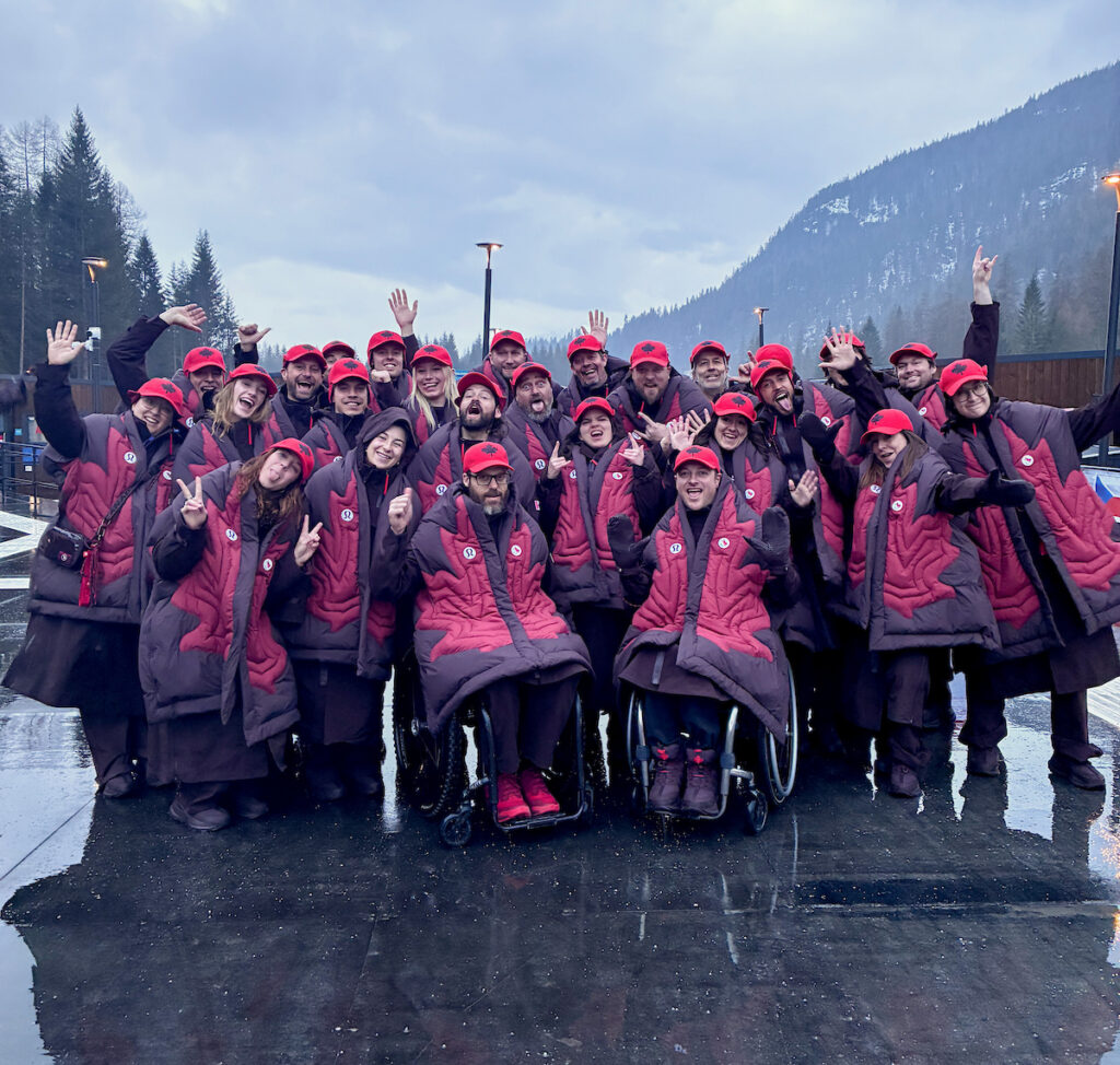 Canadian athletes gathered for a photo in red Paralympic apparel in front of a mountain background with a grey sky